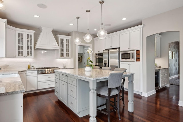 kitchen featuring a center island, stainless steel appliances, glass insert cabinets, white cabinetry, and premium range hood