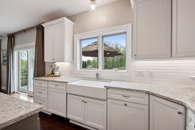 kitchen featuring dark wood finished floors, decorative backsplash, white cabinets, light stone counters, and a sink