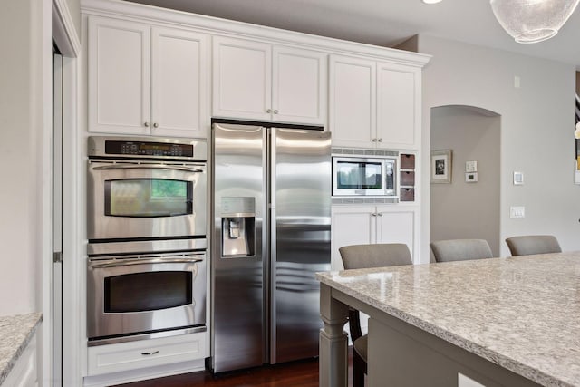 kitchen featuring arched walkways, white cabinets, light stone counters, a kitchen breakfast bar, and stainless steel appliances