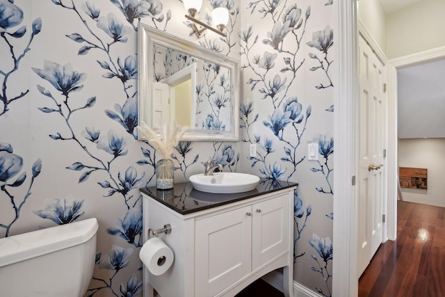 half bath featuring wood finished floors, vanity, toilet, and wallpapered walls