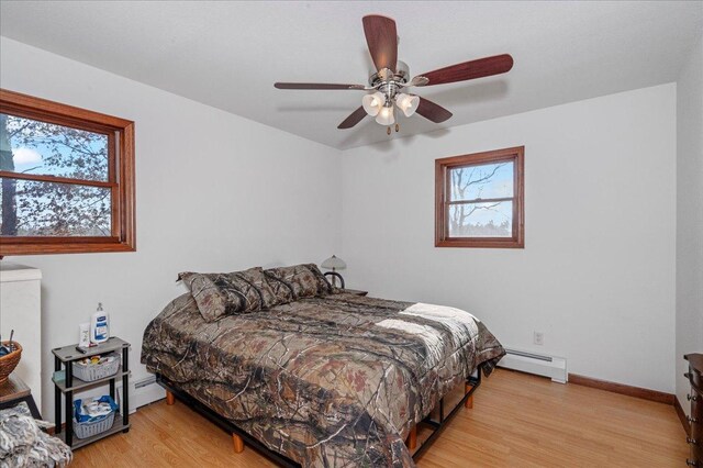 bedroom featuring ceiling fan, light wood-type flooring, and baseboard heating