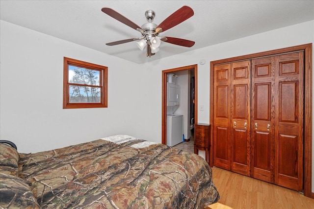 bedroom with a closet, stacked washer and clothes dryer, light hardwood / wood-style floors, and ceiling fan