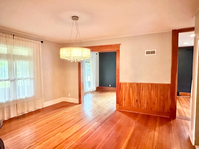 unfurnished dining area featuring wainscoting, a notable chandelier, visible vents, and wood finished floors
