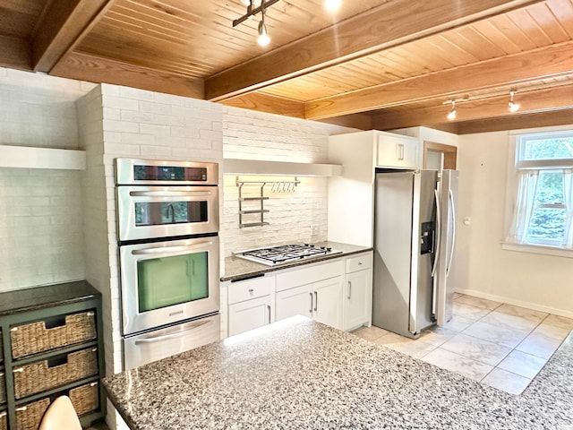 kitchen featuring white cabinets, stainless steel appliances, rail lighting, and dark stone countertops