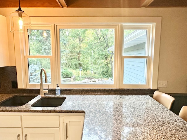kitchen with white cabinets, hanging light fixtures, dark stone counters, and a sink