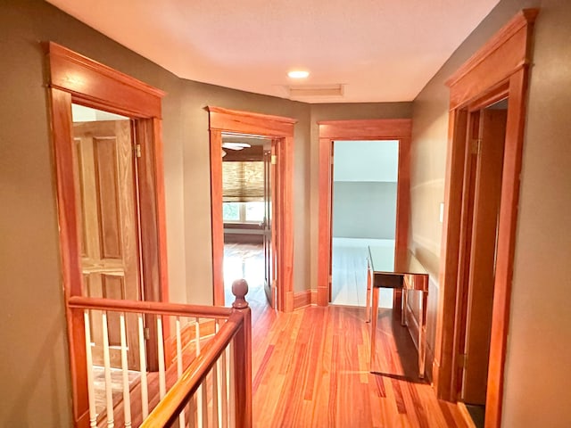 corridor with baseboards, light wood finished floors, and an upstairs landing
