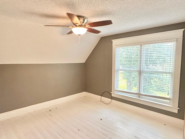 additional living space featuring a ceiling fan, vaulted ceiling, a textured ceiling, baseboards, and wood finished floors