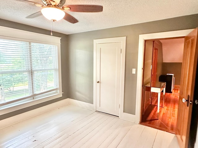 empty room with ceiling fan, a textured ceiling, and light wood finished floors