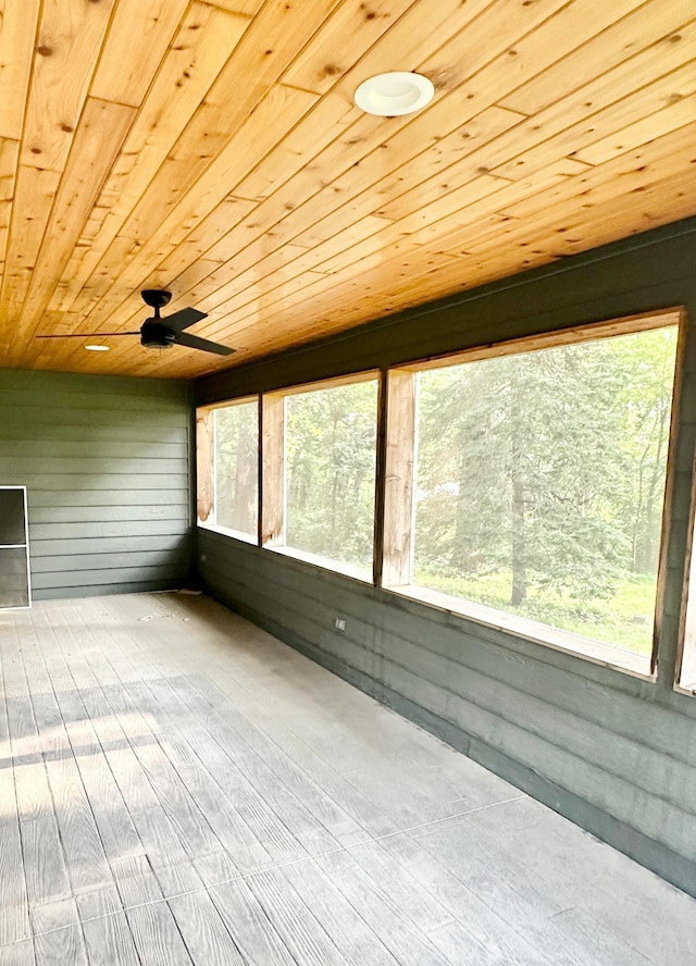 unfurnished sunroom with wooden ceiling, wood walls, a ceiling fan, and wood finished floors