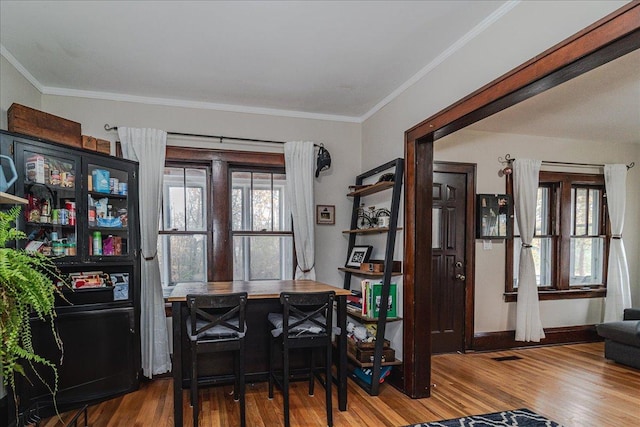 dining area featuring indoor bar, wood-type flooring, and crown molding