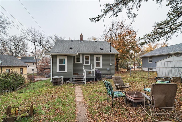 rear view of house with central air condition unit, a yard, and an outdoor fire pit