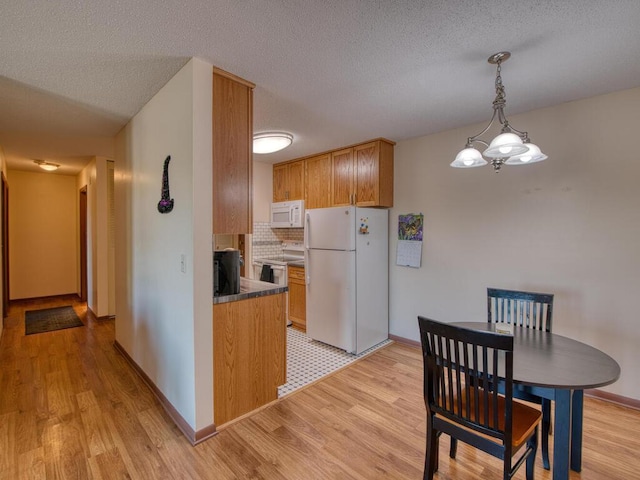 kitchen featuring white appliances, tasteful backsplash, a textured ceiling, decorative light fixtures, and light wood-type flooring