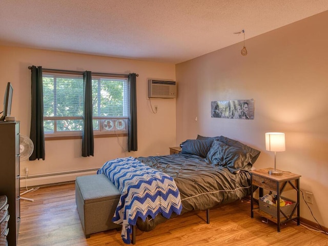 bedroom with a baseboard radiator, a textured ceiling, a wall unit AC, and light wood-type flooring