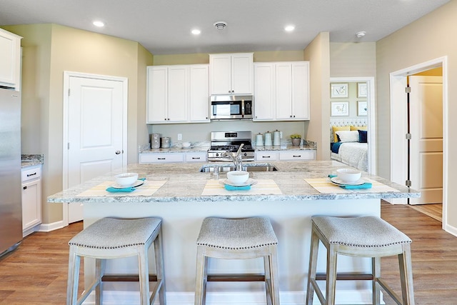 kitchen featuring white cabinetry, appliances with stainless steel finishes, a center island with sink, and a breakfast bar area