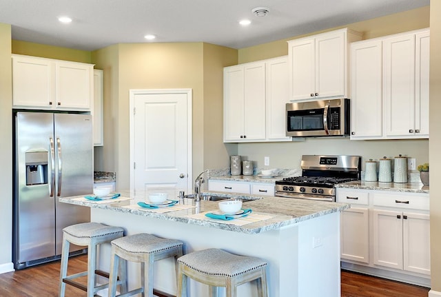 kitchen with stainless steel appliances, a kitchen island with sink, dark hardwood / wood-style flooring, white cabinets, and sink