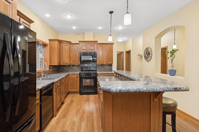 kitchen featuring tasteful backsplash, sink, black appliances, pendant lighting, and light hardwood / wood-style flooring