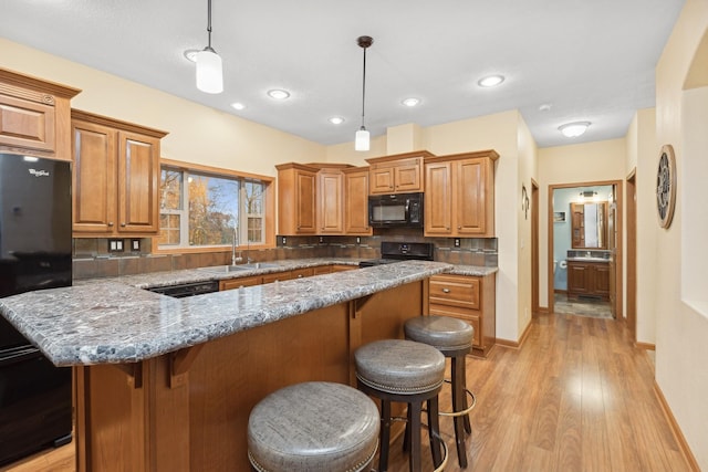 kitchen with black appliances, pendant lighting, a center island, light hardwood / wood-style floors, and a breakfast bar area