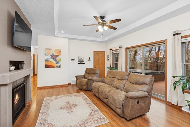 living room featuring light wood-type flooring, a tray ceiling, and ceiling fan