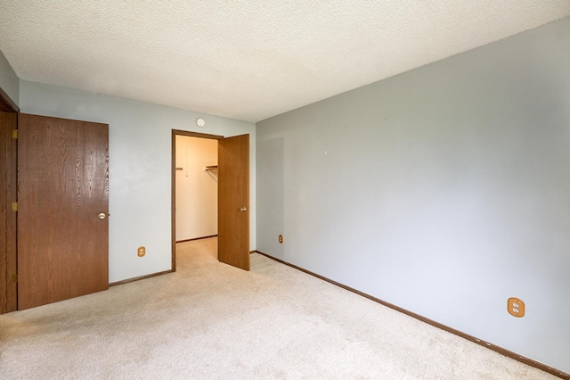 unfurnished bedroom featuring light carpet, a spacious closet, a closet, and a textured ceiling