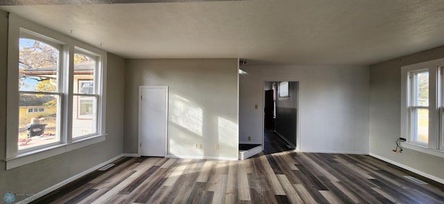 empty room with a wealth of natural light and dark hardwood / wood-style flooring