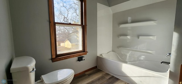 bathroom with toilet, a tub to relax in, hardwood / wood-style flooring, and a wealth of natural light