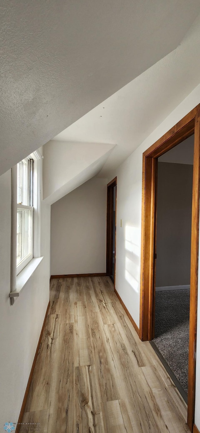 bonus room with light hardwood / wood-style floors, a textured ceiling, and lofted ceiling