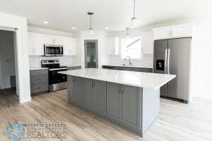 kitchen with white cabinets, a kitchen island, appliances with stainless steel finishes, pendant lighting, and gray cabinetry