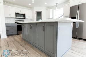 kitchen with appliances with stainless steel finishes, gray cabinets, decorative light fixtures, and white cabinets