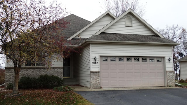 view of front of property featuring brick siding, a garage, roof with shingles, and driveway