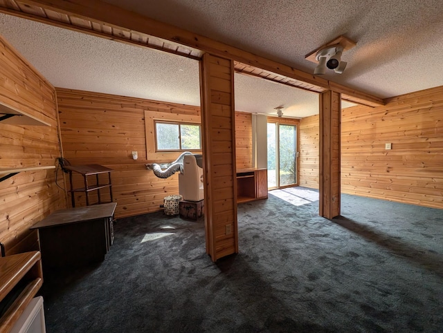 interior space with dark carpet, wooden walls, and a textured ceiling