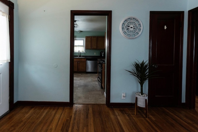 corridor with dark wood-type flooring, a sink, and baseboards