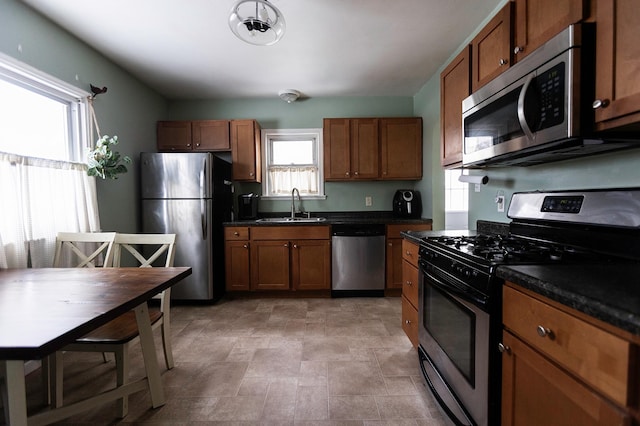 kitchen with appliances with stainless steel finishes, dark countertops, a sink, and brown cabinets