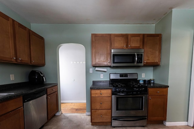 kitchen with brown cabinetry, baseboards, arched walkways, and stainless steel appliances