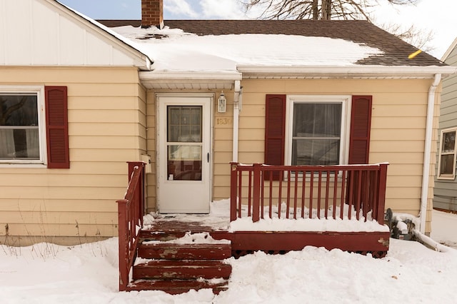 snow covered property entrance featuring a shingled roof, a porch, and a chimney