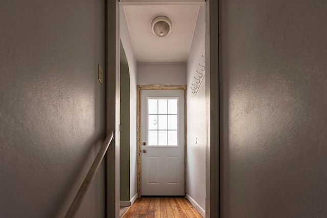 doorway featuring a textured wall, light wood finished floors, and baseboards