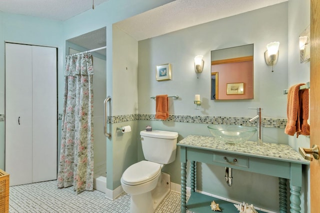 bathroom with tile patterned floors, toilet, curtained shower, a textured ceiling, and sink