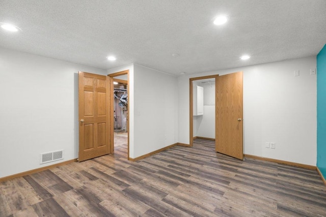 unfurnished bedroom with a walk in closet, a closet, dark wood-type flooring, and a textured ceiling