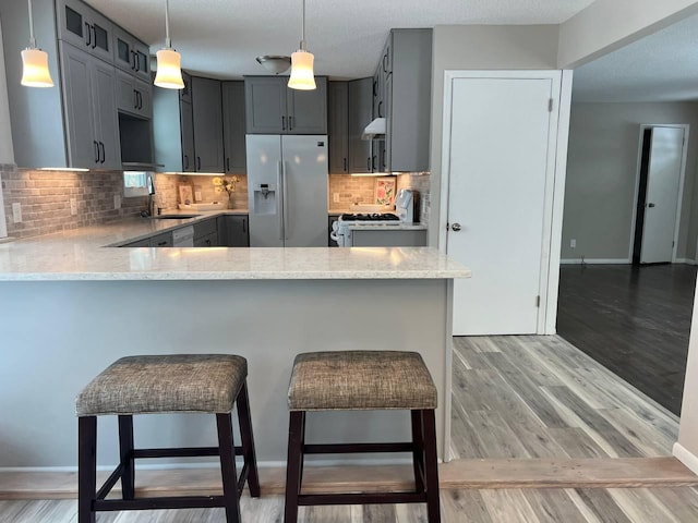 kitchen featuring light wood finished floors, light stone counters, stove, a peninsula, and refrigerator with ice dispenser