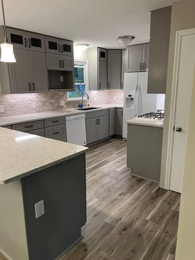 kitchen featuring tasteful backsplash, light wood-style flooring, gray cabinetry, a sink, and white appliances