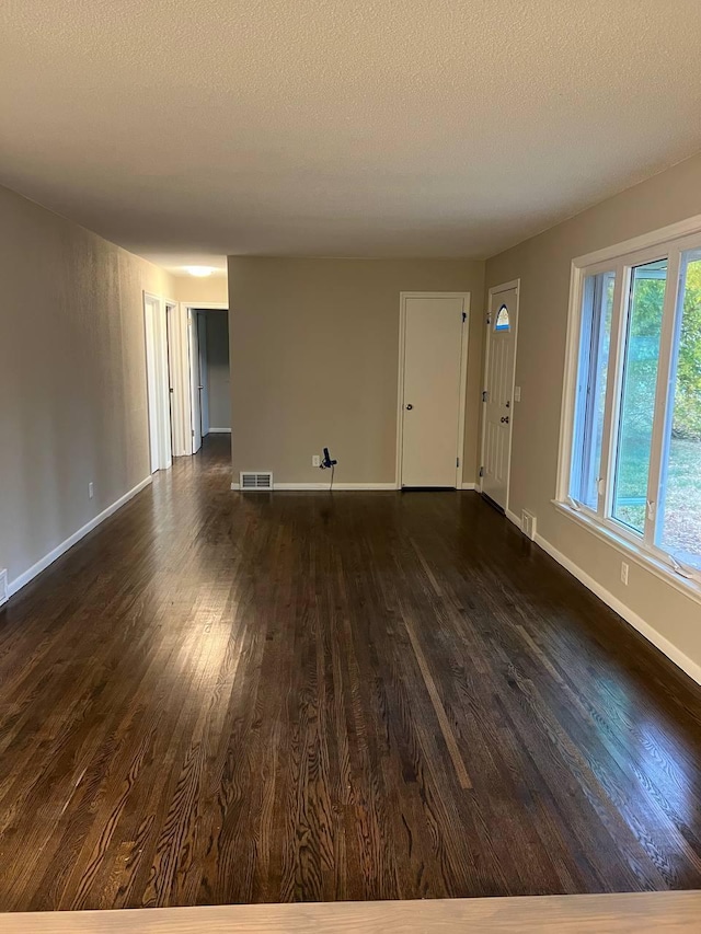 unfurnished living room featuring dark wood-style flooring, visible vents, a textured ceiling, and baseboards