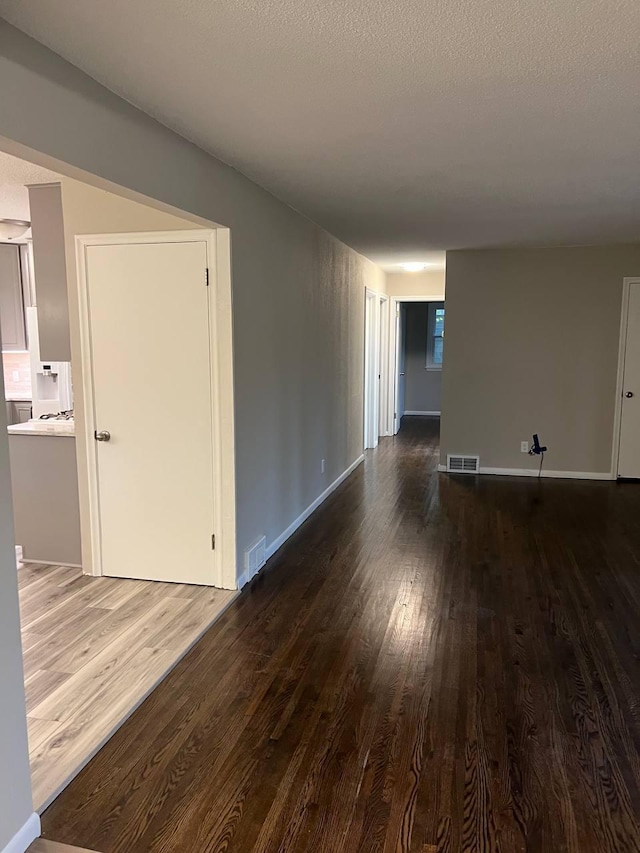 empty room with visible vents, a textured ceiling, baseboards, and wood finished floors