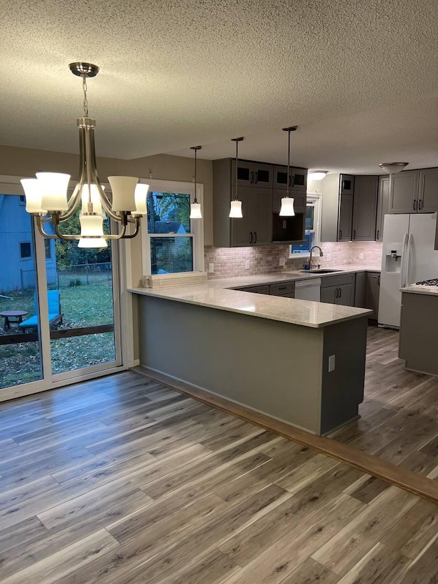 kitchen featuring backsplash, a sink, wood finished floors, white appliances, and a peninsula