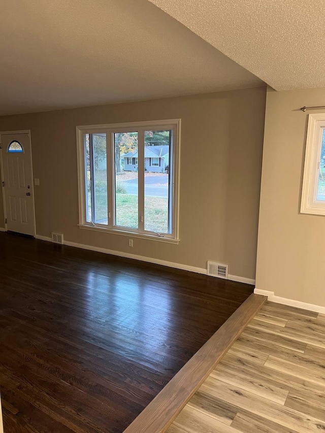 unfurnished living room featuring visible vents, baseboards, and wood finished floors