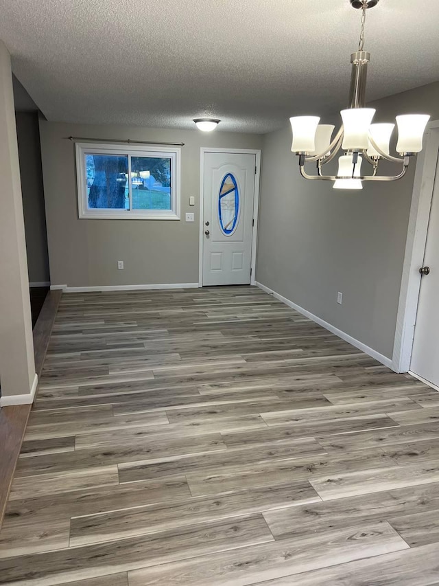 entrance foyer with a chandelier, a textured ceiling, wood finished floors, and baseboards