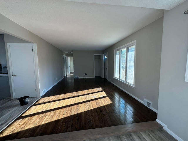 unfurnished living room with wood finished floors, visible vents, and baseboards