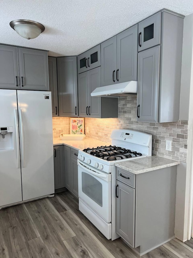 kitchen featuring gray cabinets, white appliances, under cabinet range hood, and wood finished floors