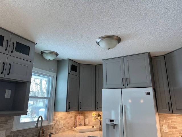 kitchen with tasteful backsplash, gray cabinets, light countertops, white fridge with ice dispenser, and a sink