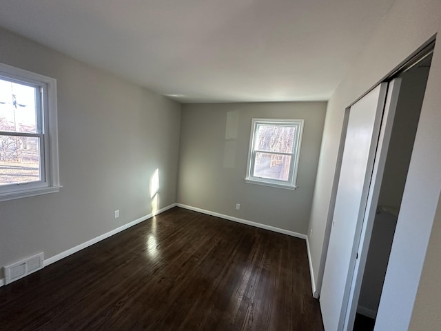 unfurnished bedroom featuring a closet, visible vents, dark wood finished floors, and baseboards