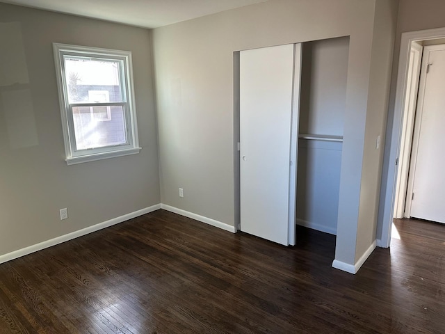 unfurnished bedroom featuring dark wood-style floors, baseboards, and a closet