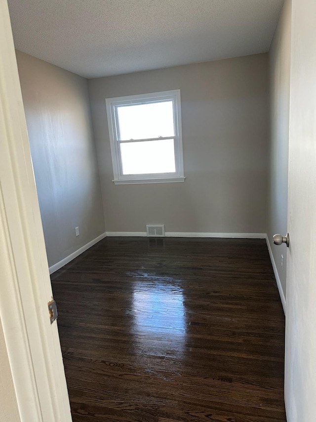 empty room with dark wood-style flooring, visible vents, a textured ceiling, and baseboards